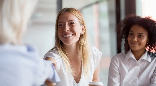Woman with blonde hair smiles and shakes hands with another person