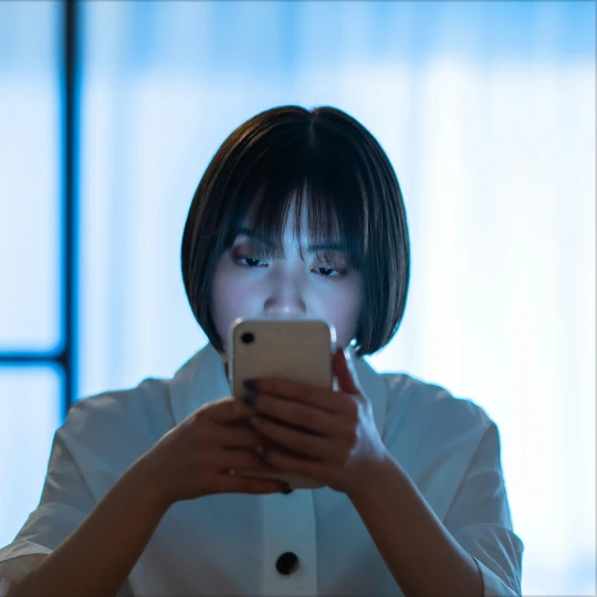 A businesswoman with short dark hair, wearing a white blouse, is holding a smartphone.
