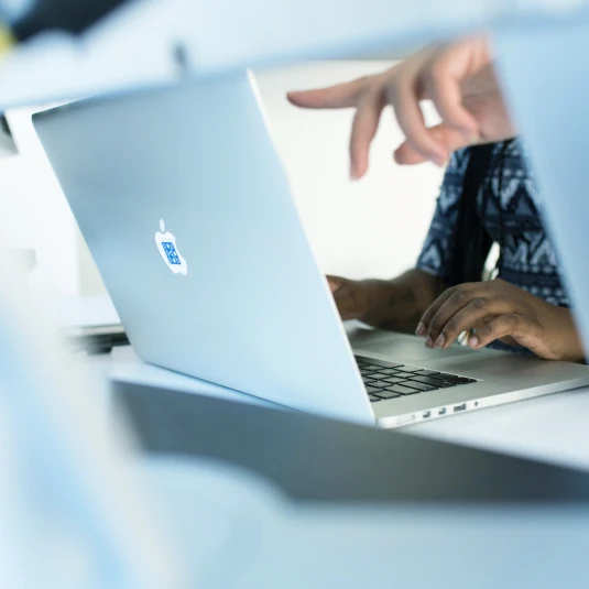 Person’s hand pointing to something on a laptop screen, indicating a detail or explaining information.