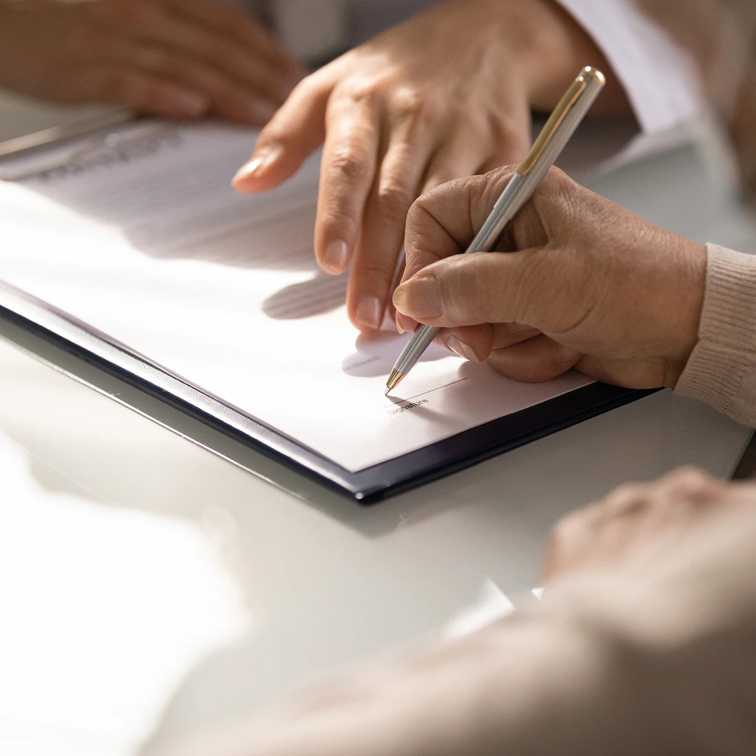 Close-up of a person signing a document, with another hand assisting, suggesting a contract or agreement