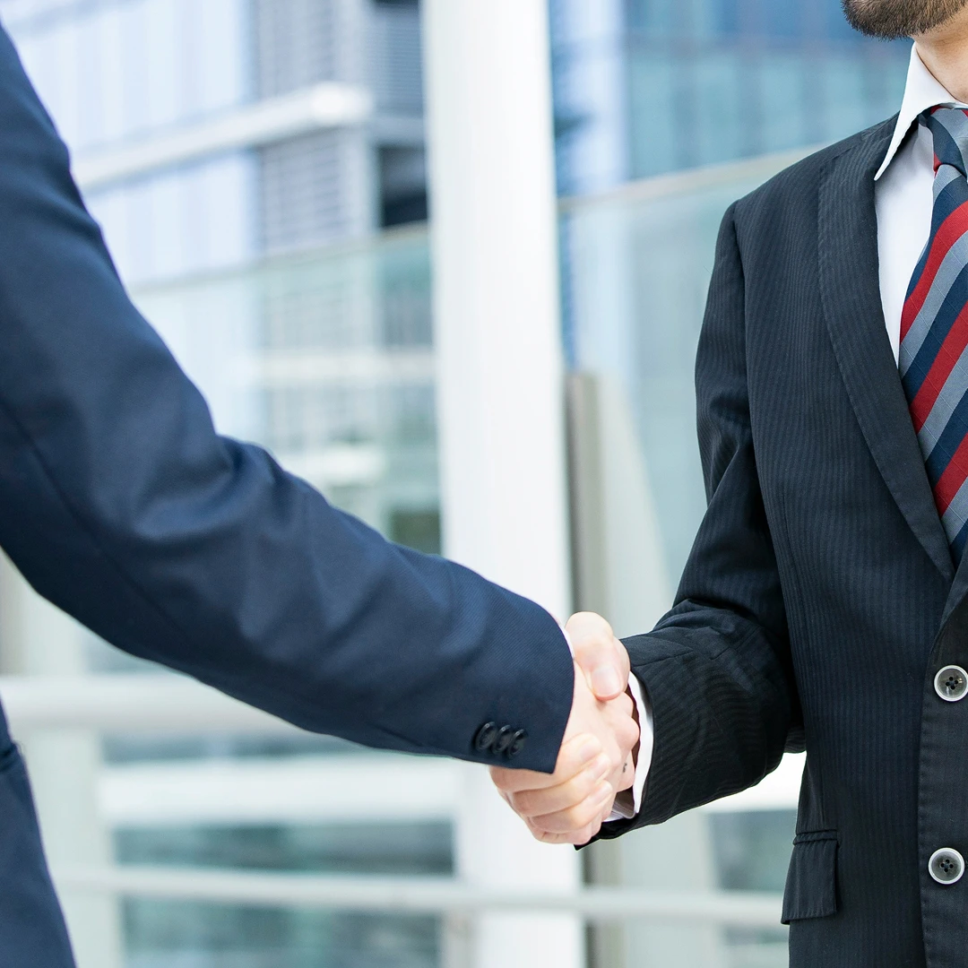 Business professionals in suits shaking hands in front of a modern building