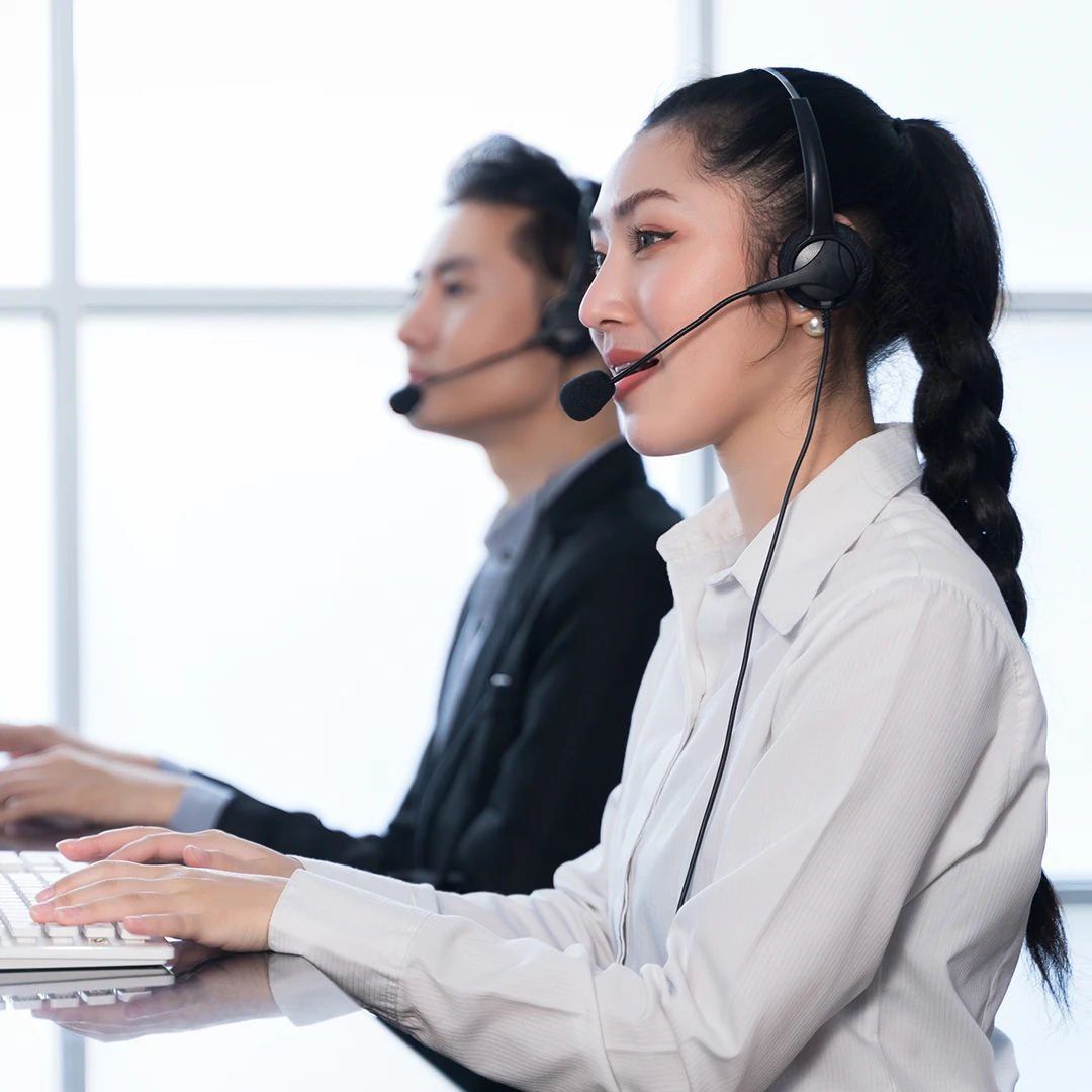 Two customer service representatives, a woman and a man, wearing shirts and headsets, working at their desks
