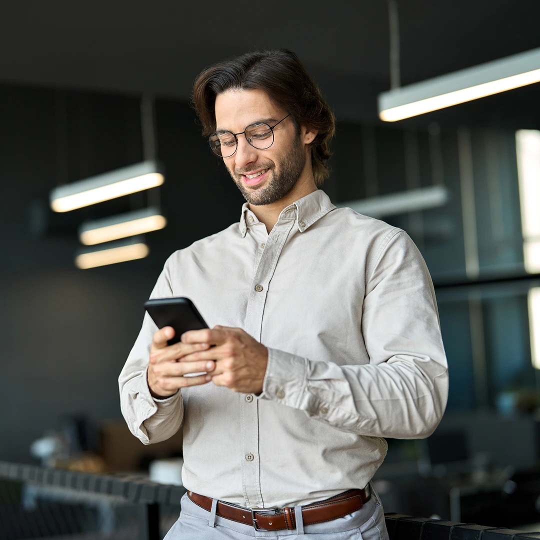A man smiling while using his phone in the office