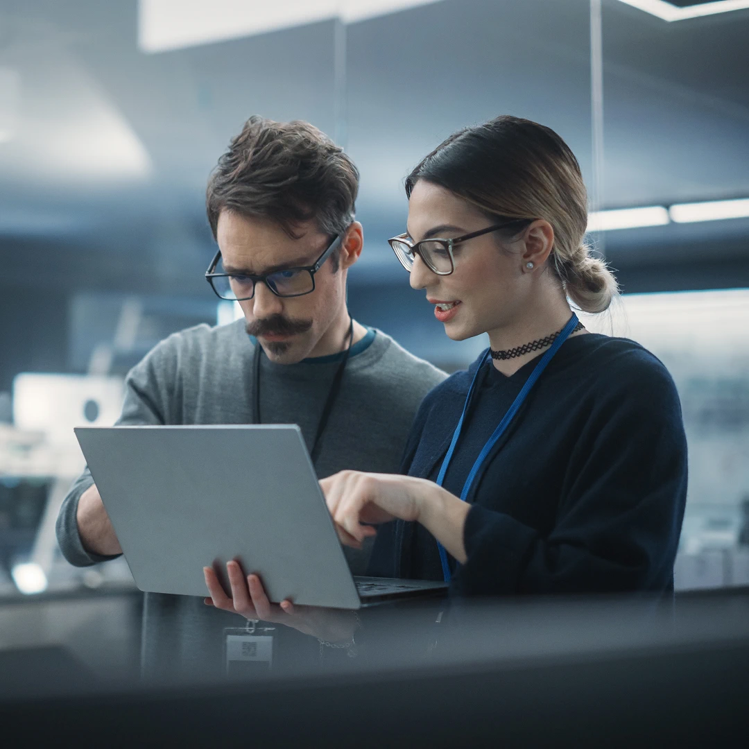 Man and woman in glasses collaborating on a laptop