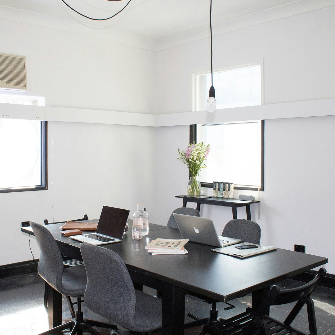 Bright and minimalist conference room with a dark table, laptops, and a vase of flowers