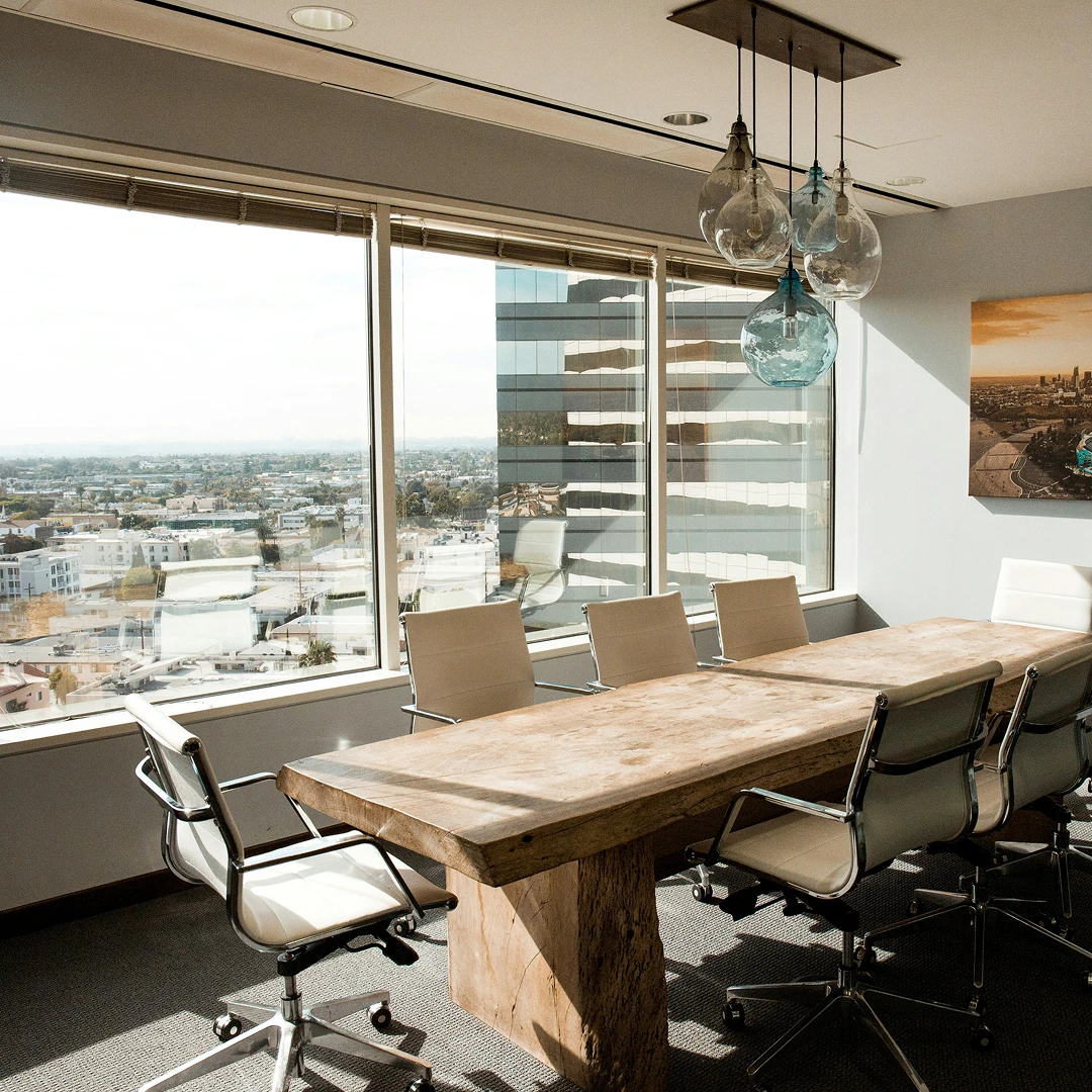 A modern conference room with a large wooden table, leather chairs, and a panoramic city view