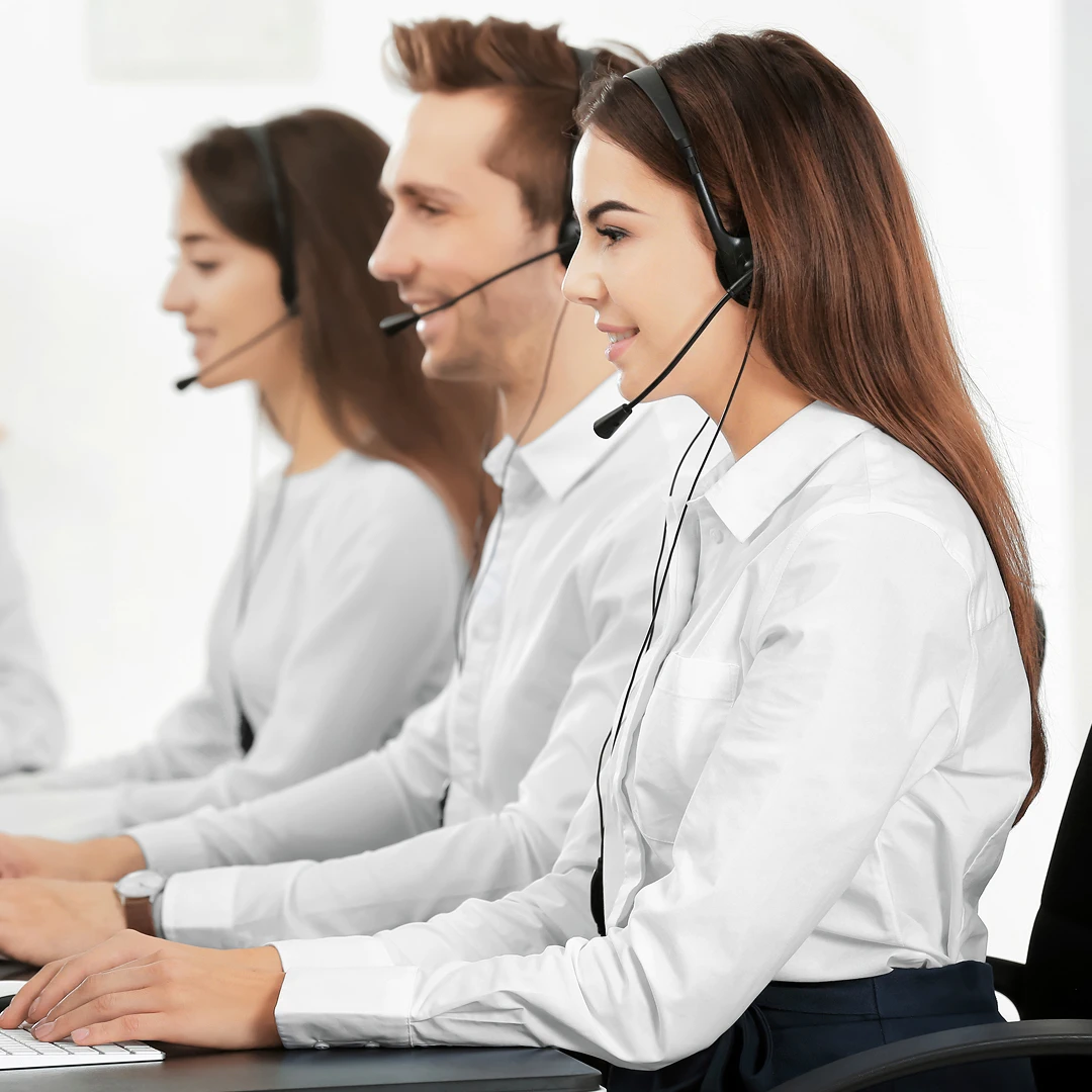 Team of customer service representatives, two women and a man, wearing white shirts and headsets, focused on assisting customers in a call center setting