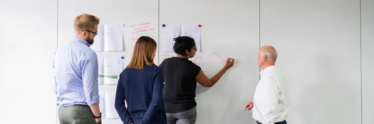 a group of people, one lady drawing something on a wall with a red marker